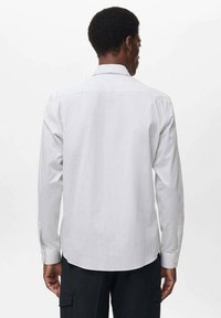 Camisa blanca de manga larga con finas rayas verticales, cuello abotonado y espalda lisa. Presenta una textura suave y puños estándar.