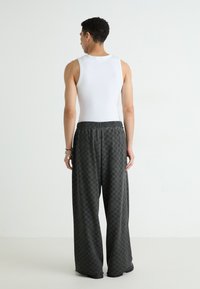 White sleeveless tank top paired with loose black checkered pants, featuring a drawstring waist and subtle texture. View from the back.
