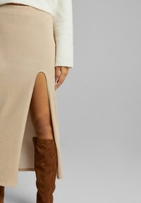 Beige ribbade kjolen med hög slits, ihop med bruna över-knä stövlar. Kjolen har en åtsittande passform och textil med struktur.