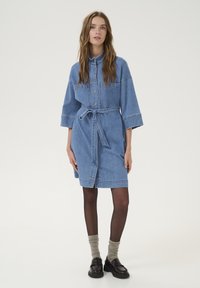 Denim shirt dress with a collar, short sleeves, button-down front, and waist tie. Light blue color with subtle stitching details.