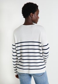 Pull à manches longues avec un corps blanc et des rayures horizontales bleu marine, fabriqué dans un matériau tricoté doux, avec une coupe décontractée et un col rond.