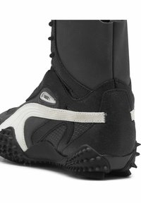Zwarte sportieve laars met een hoge schacht, voorzien van een witte streep, gestructureerd suède en rubberen spikes op de zool voor optimale grip.