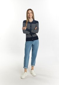 Marine gestreifter, langärmeliger Cardigan mit weißen Streifen und knöpfbarem Frontbereich. Kombiniert mit hochgekrempelten hellblauen Jeans und weißen Sneakers.