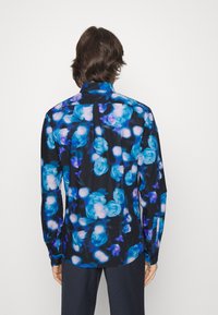 Camisa de manga larga con una base negra y un vibrante patrón floral azul. Fabricada en tejido ligero, con puños abotonados y un dobladillo recto.