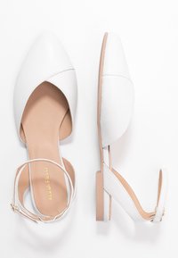 Białe płaskie buty z ostrym noskiem, paskiem na kostce i jasnobeżową wyściółką. Gładki materiał przypominający skórę z minimalistycznym wzornictwem.