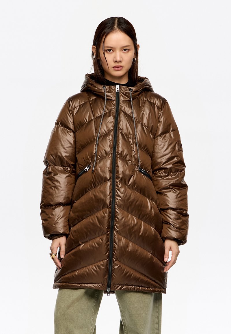 Brązowa puchowa kurtka z pikowanym wzorem w jodełkę, kapturem, dwoma zapinanymi na zamek bocznymi kieszeniami oraz zamkiem błyskawicznym na całej długości. Faktura błyszcząca, o wyraźnym wykończeniu.