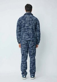 Ensemble de veste et pantalon bleu marine présentant un motif géométrique texturé dans des nuances variées de bleu. Fabriqué à partir d'un tissu résistant, conçu pour la polyvalence.