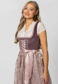 Traditional dirndl dress featuring a lavender velvet bodice with lace-up detail, satin ribbon belt, and a sheer, patterned pink skirt.