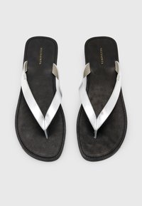 Sandali neri piatti con una morbida texture in suede, caratterizzati da cinturini metallici argento a forma di V e un'estetica minimalista.