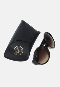 Óculos de sol com gradiente castanho, lentes redondas grandes, com detalhes em preto, e uma bolsa de couro preta com um logotipo dourado.