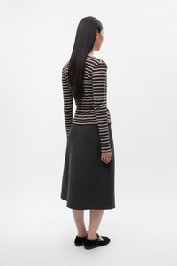 Gestreept bruin-wit top met lange mouwen gecombineerd met een donkergrijze, luchtige rok, aangevuld met zwarte schoenen met een cirkelvormig accent.