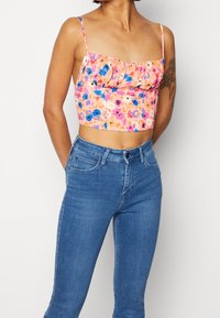 Kwiatowy top z falbaną przy dekolcie, w różowych, niebieskich i pomarańczowych wzorach. W zestawie z dopasowanymi niebieskimi dżinsami.