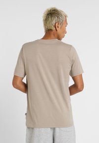 Camiseta de manga corta beige, hecha de tela suave, con un cuello redondo clásico y un corte relajado. No se ven logotipos o patrones destacados.