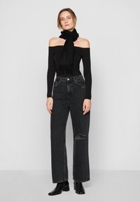 Svart avskuren topp, högmidjade svarta jeans i denim med ett hål vid knäet, och svarta ankelstövlar. Svart scarf med fransar.