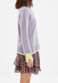 Maglione lavorato a maglia lilla con motivo a trecce e polsini a coste gialli, abbinato a una mini gonna nera floreale con orlo arricciato.