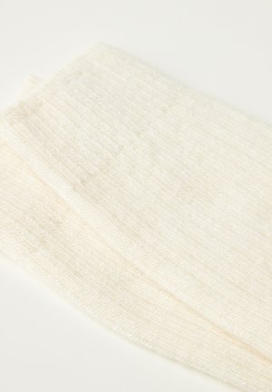 Krämfärgad, ribbad stickad tygsektion som visar en mjuk textur och subtila variationer i vävning, med en svag lyster.