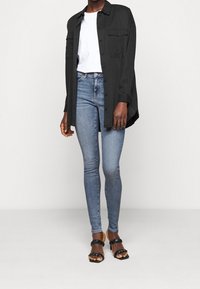 Černá košile s knoflíky přes bílý tričko, k tomu středně modré skinny džíny a černé sandály na silné pásky.