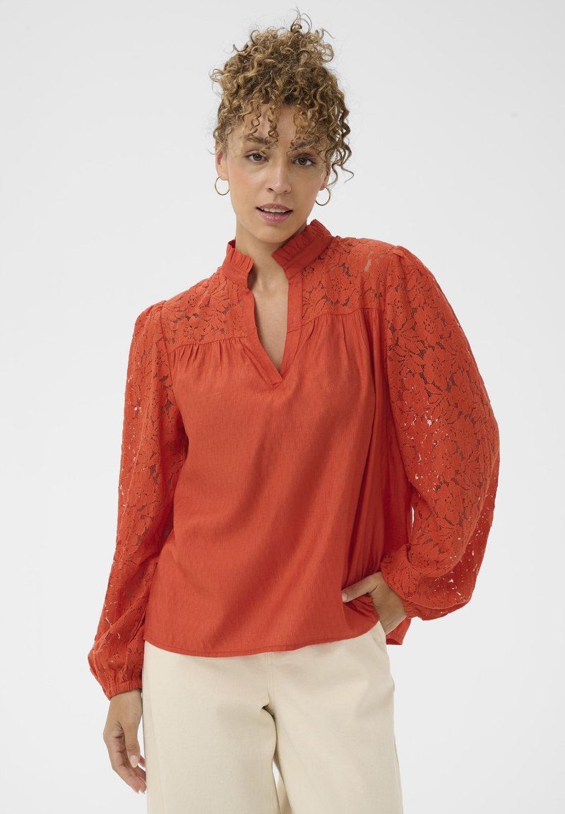 Blouse rouge à col montant, avec des manches en dentelle et un corps texturé. Manches longues et amples, coupe décontractée.
