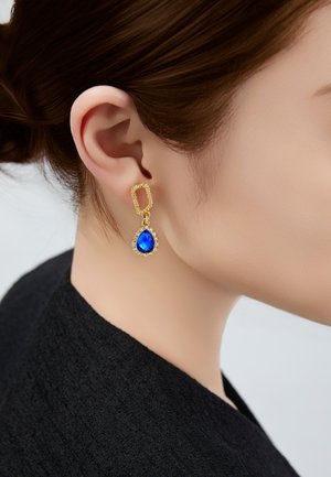 Goldene Tropfenohrringe mit einem blauen, facettierten Stein, umgeben von kleinen, klaren Steinen, die an einer strukturierten rechteckigen Rückseite befestigt sind.