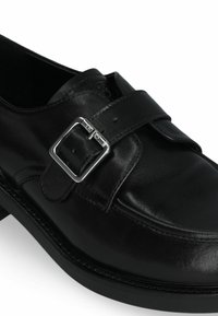 Schwarzes Leder Schuh mit einer abgerundeten Zehe, ausgestattet mit einem breiten Riemen, der mit einer silbernen Schnalle gesichert ist. Glatte Textur und niedriger, stabiler Absatz.