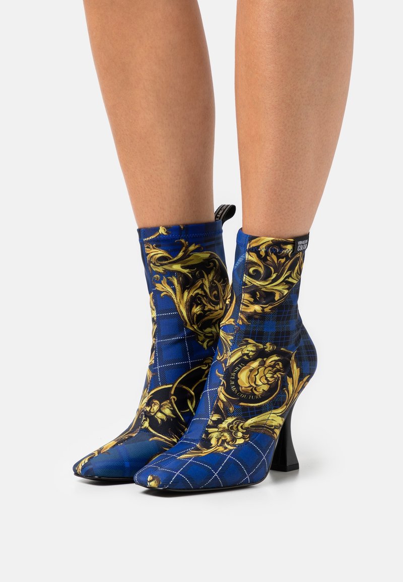 Bottes chevilles à bout pointu en motif bleu et or, présentant un design à carreaux avec des accents floraux, finition avec un talon moyen noir.