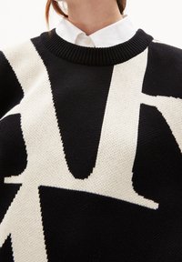 Sweter dzianinowy z czarno-kremowym geometrycznym wzorem, okrągłym dekoltem i ściągaczami. Tekstura jest miękka i oddychająca.