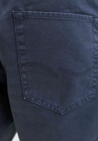 Σκούρο μπλε denim ύφασμα με ραμμένη πίσω τσέπη που διαθέτει ένα διακριτικό καμπυλωτό σχέδιο με ραφή στο πάνω μισό.