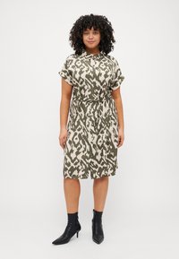 Button-up dress featuring a light olive green and cream abstract pattern, short sleeves, cinched waist, and knee-length hem. Black ankle boots.
