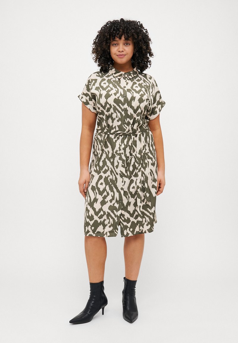 Button-up dress featuring a light olive green and cream abstract pattern, short sleeves, cinched waist, and knee-length hem. Black ankle boots.