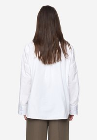Biała koszula z długim rękawem o luźnym kroju, z karczkiem z tyłu, guzikami przy mankietach i gładką bawełnianą fakturą.