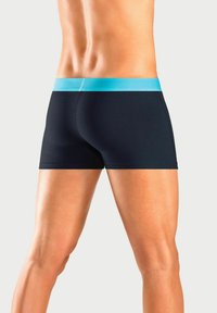 Black boxer briefs with a turquoise waistband, featuring a smooth texture and fitted design that enhances leg definition.