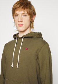 Felpa verde oliva realizzata in tessuto morbido, dotata di una tasca frontale, cappuccio con cordoncino e un piccolo logo rosso di Levi's sul petto.