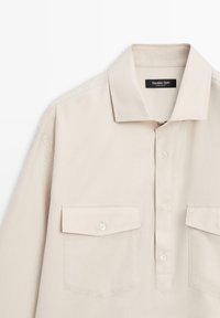 Chemise beige à manches longues avec col, boutons sur le devant et deux poches à rabat boutonnées, étiquetée Massimo Dutti, fabriquée en Égypte.
