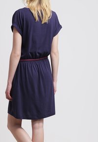 Granatowa sukienka z krótkim rękawem, o luźnym kroju i elastycznym pasie. Miękka tkanina o gładkiej fakturze, kończąca się tuż nad kolanem.
