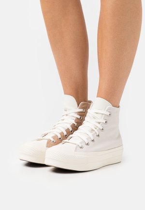 Zapatillas altas de lona blanca y beige, con cordones blancos, puntera redonda, suela de goma texturizada y ojales metálicos.