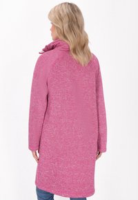 Giacca rosa a maniche lunghe con tessuto strutturato, con colletto alto e vestibilità rilassata, che arriva fino a metà coscia, senza chiusure visibili.