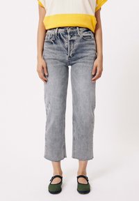 Vervaagde blauwe high-waisted jeans met een rechte pijp, verweringdetails, rafelige zoom, gecombineerd met groene schoenen en een top met gele accenten.
