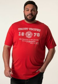 Camiseta de algodón roja con texto gráfico blanco, mangas cortas y cuello redondo. El diseño incluye detalles temáticos de pesca y acentos de logotipo.