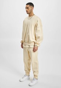 Beige oversized collegepusero ja siihen sopivat verkkarit pehmeästä materiaalista, joissa on uurrettuja hihansuita ja joustovyötärö. Asusteena valkoiset lenkkarit.