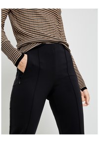 Svarta åtsittande byxor med fickor med blixtlås och en slät yta, i kombination med en brunrandig långärmad topp som har kontrasterande ärmslut.