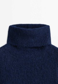 Pull à col roulé en tricot duveteux bleu marine avec un col épais et doux, plié de manière uniforme.