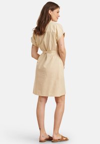 Beiges Leinenkleid mit kurzen Ärmeln, tailliertem Schnitt und knieumspielendem Saum. Es zeichnet sich durch ein simples, klares Design und eine glatte Textur aus.