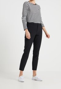 Černé kalhoty s úzkým střihem, s poutky na opasek a hladkou texturou, ve spojení s černo-bílým pruhovaným dlouhým rukávem. Bílé tenisky.