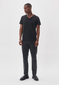 T-shirt nera a scollo a V in un tessuto morbido abbinata a jeans slim-fit grigio scuro e mocassini neri, creando un outfit casual.