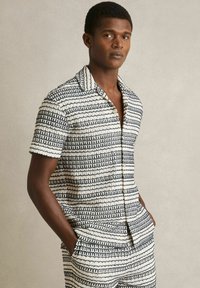 Cămașă cu mâneci scurte, cu nasturi, având un design texturat din tricot, cu dungi orizontale alternative negre și albe și un guler moale.