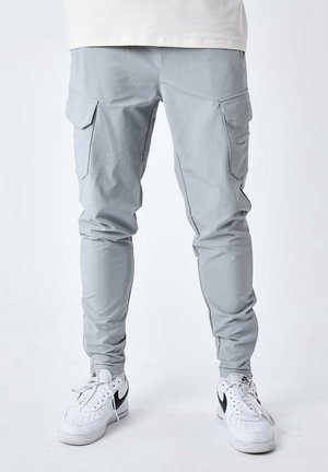 Pantalons cargo gris clair avec des jambes fuselées, des poignets élastiques, des poches latérales et une texture lisse, associés à des baskets blanches avec des accents noirs.