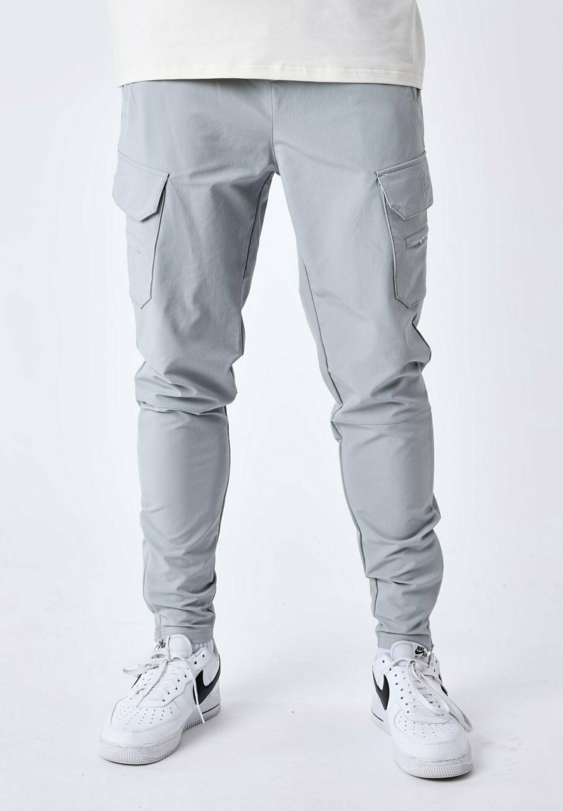 Pantalones cargo gris claro con piernas ajustadas, puños elásticos, bolsillos laterales y una textura suave, combinados con zapatillas blancas con acentos negros.