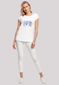 Hvit t-skjorte med korte ermer og rund hals som har et fargerikt vinter-tema grafikk. Kombinert med hvite skinny jeans og hvite joggesko.