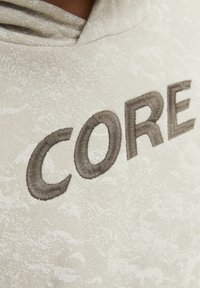 Světle šedá mikina s kapucí vyrobená z texturované tkaniny, s vyšitým nápisem "CORE" v tmavě šedé barvě na přední straně. Kapuce je viditelná nahoře.