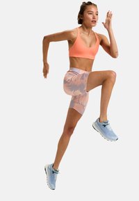 Sportoutfit mit einem pinken Sport-BH und gemusterten, hellen Shorts. Hellblaue Laufschuhe runden das Ensemble ab.